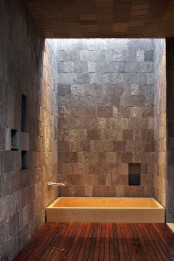 a rustic bathroom with stone walls and a wooden floor plus a built-in bathtub and a skylight
