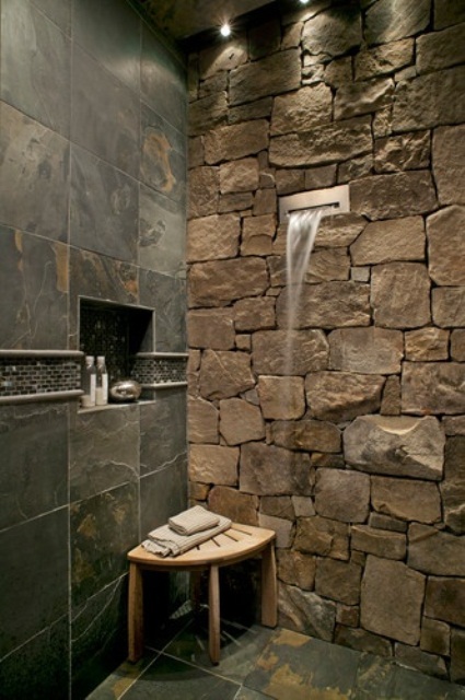 a natural shower space with a stone wall and dark tiles that imitate dark stone, too