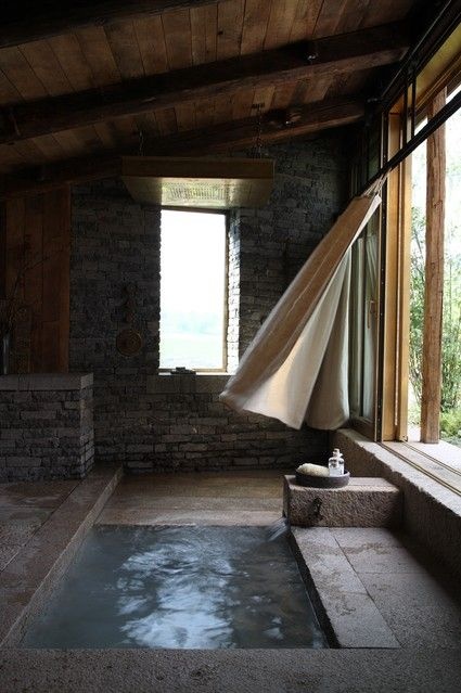 an outdoor-indoor bathroom with stone walls and a floor plus a built-in bathtub