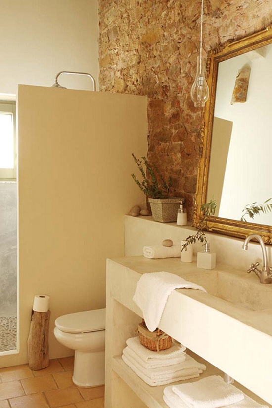 a warm neutral bathroom done with stone, concrete and tiles on the floor plus some touches of greenery