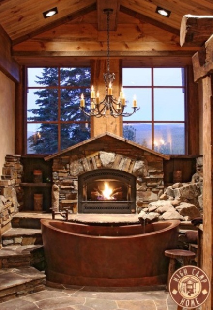 a gorgeous cabin bathroom with decorative stone, a metal tub, a fireplace and a view will make you spend hours here