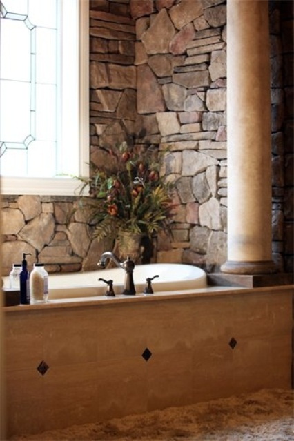 natural stone walls and a bathtub clad with light-colored wood plus a pillar for a chic eclectic look