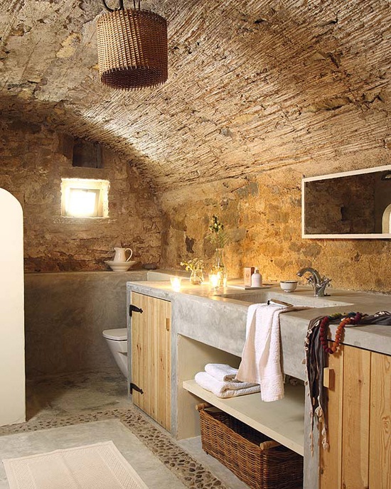 a wabi-sabi bathroom with stone walls, concrete and wood furniture and a wicker lampshade