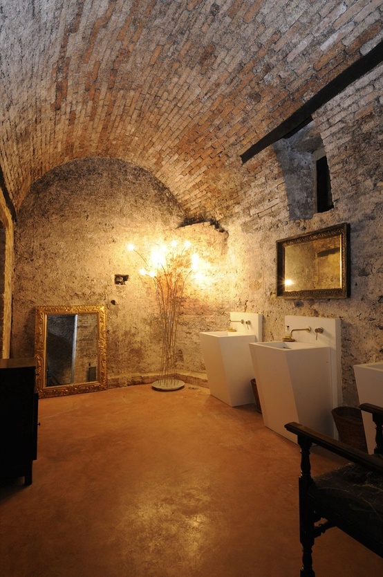 a unique bathroom with whitewashed stone walls and an arched ceiling, a concrete floor and modern appliances