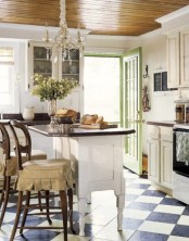 a white vintage kitchen with a checked floor, vintage white cabinetry, a white vintage kitchen island and vintage stained chairs