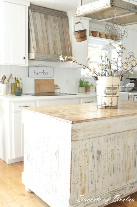 a white farmhouse kitchen with a shabby chic wooden kitchen island made of a cabinet, a reclaimed wooden hood and modern appliances and fixtures