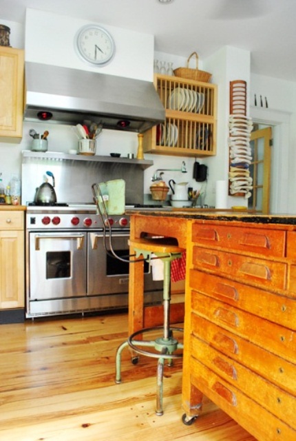 a light-stained kitchen with stainless steel appliances and a kitchen island made of a vintage industrial desk for a unique look