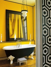 a bright and chic yellow and black bathroom with a large mirror in a black frame, a black clawfoot bathtub, yellow walls with black edges and a pendant lamp