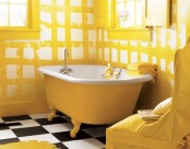 a small yellow and white printed bathroom with a black and white tiled floor, a yellow clawfoot bathub, a yellow chair and some artwork