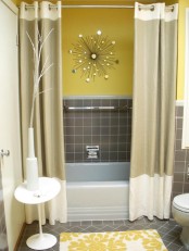 an eye-catchy bathroom with yellow and grey decor, with taupe tiles and yellow walls, matching curtains and a yellow printed rug