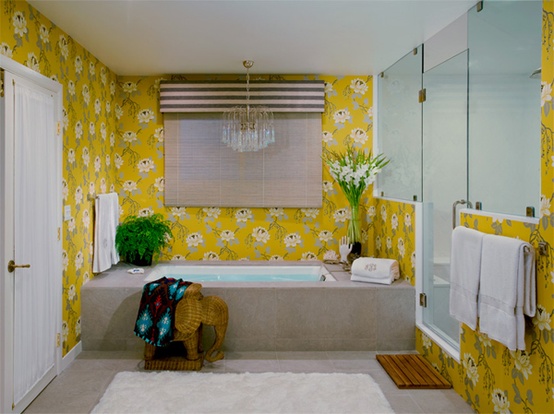 a bold bathroom with yellow floral wallpaper, a shower space enclosed in glass, a bathtub clad with concrete, a crystal chandelier