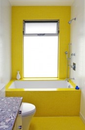 a modern small bathroom clad with bold sunny yellow tiles, a white vanity and appliances and a large window with frosted glass