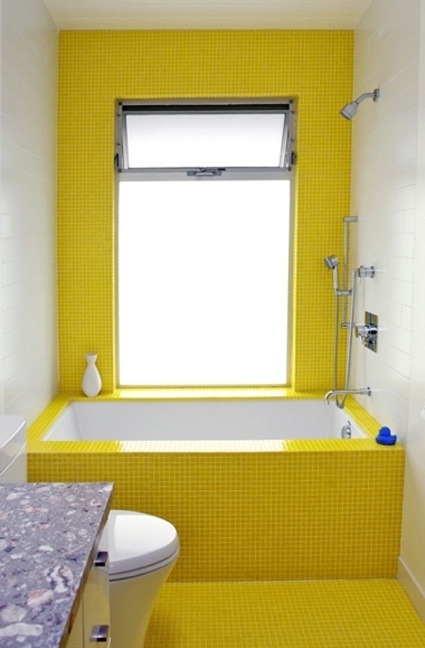 a modern small bathroom clad with bold sunny yellow tiles, a white vanity and appliances and a large window with frosted glass