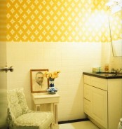 a small bathroom clad with white square tiles and yellow printed wallpaper, a vanity with a sink, some chairs and stools is a cool space with bright color