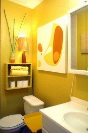 a small yet chic bathroom with mustard walls, a box shelf on the wall, artwork and white appliances