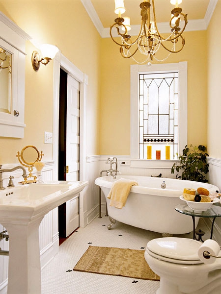 a beautiful vintage bathroom with yellow walls, a clawfoot bathtub, a vintage free-standing sink, a mosaic window and a chic chandelier